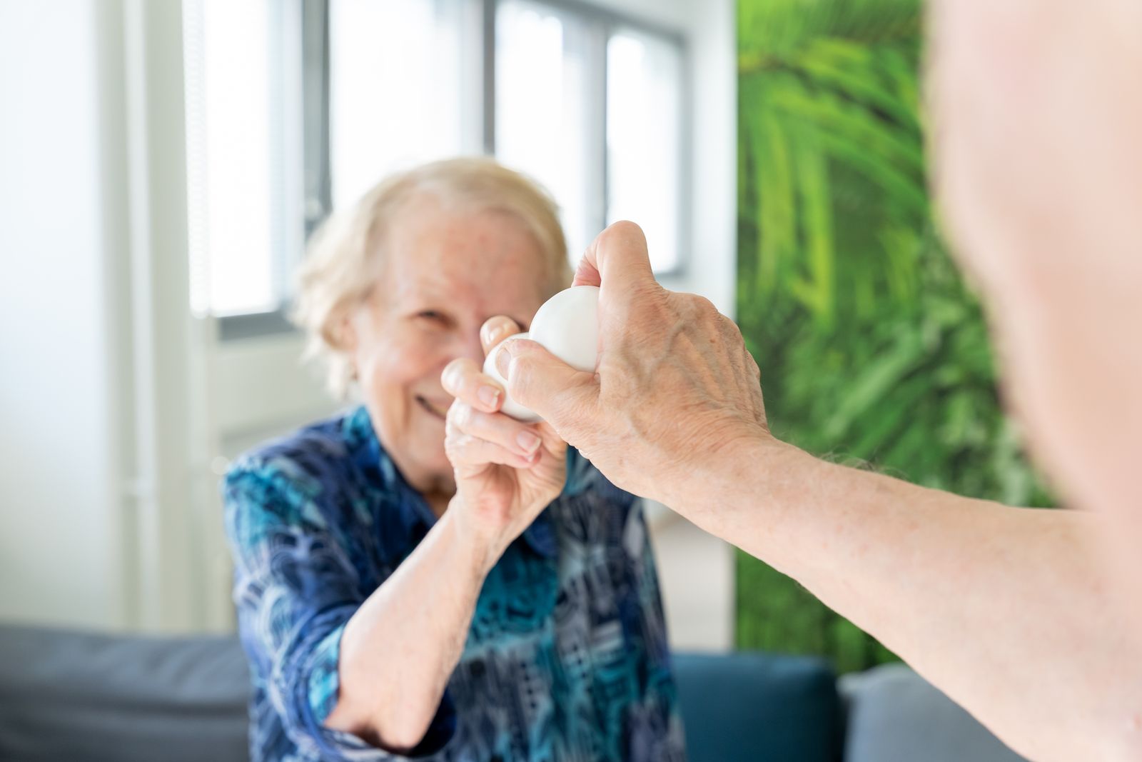 An older woman smiles as she reaches her PALL0 ball toward another person’s